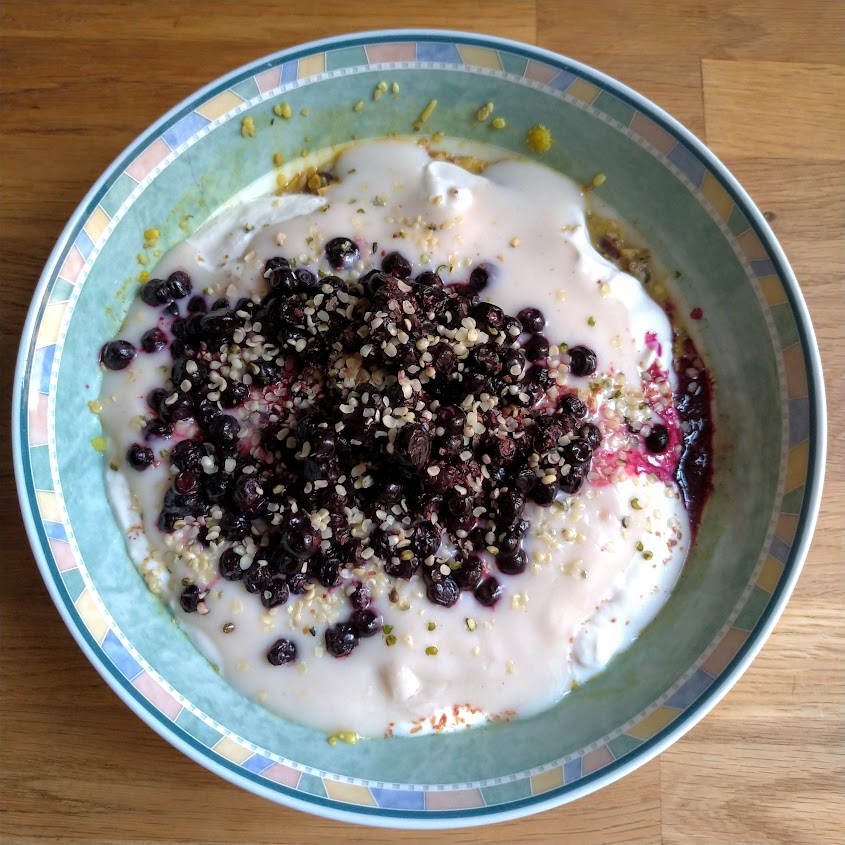 Bowl of porridge topped with creamy soya yogurt, blueberries and hemp seeds