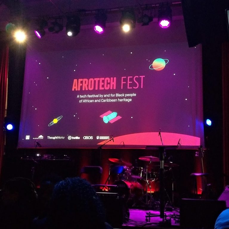 Opening slide that reads 'Afrotech Fest: A tech festival by and for Black people of African and Caribbean heritage'. On an illustrated space background with colourful planets and satellites. Sponsor logos appear at the bottom of the slide, but they're fuzzy and not legible in the photo