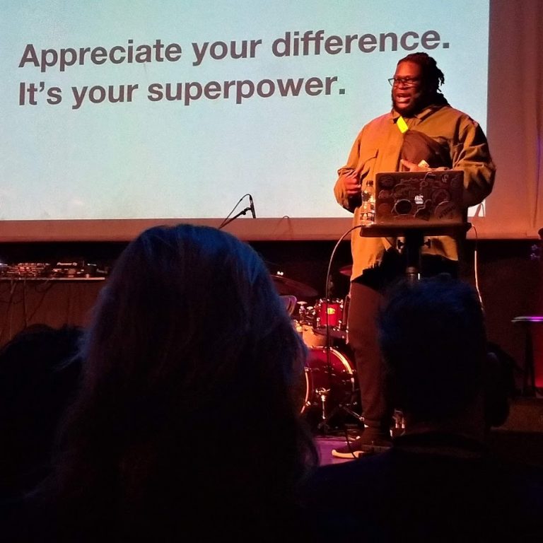 Alex Fefegha appears in front of a slide that reads: Appreciate your difference. It's your superpower.